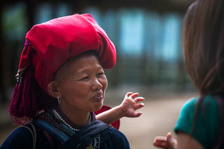 Red Dao vrouw uit Y Linh Ho bij Sapa in traditionele klederdracht, met karakteristieke rode hoofddoek en handgemaakte sieraden tijdens een ontmoeting met reizigers