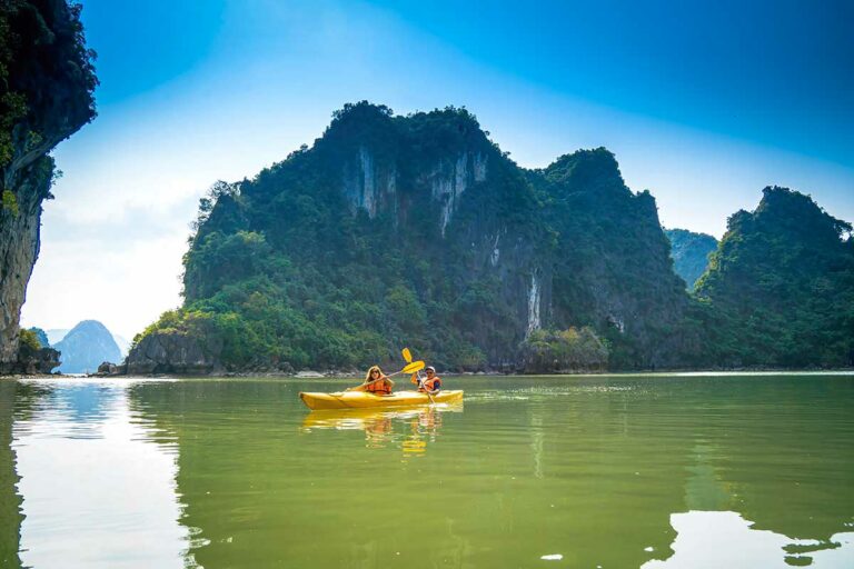 Twee reizigers kajakken door het rustige water van Lan Ha Bay, omringd door steile kalkstenen eilanden en groene kliffen tijdens een cruise bij Cat Ba Island