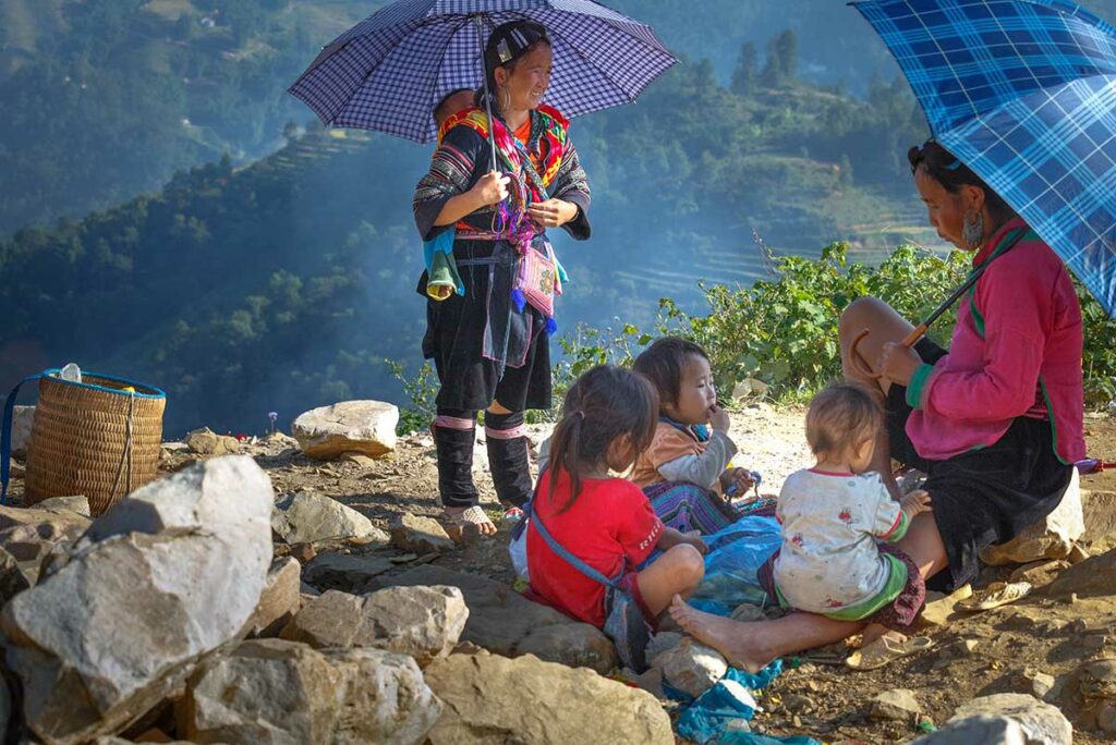 Etnische vrouwen en kinderen uit de regio Sapa rusten langs een bergpad, een intiem moment voor documentaire en portretfotografie in Noord-Vietnam.