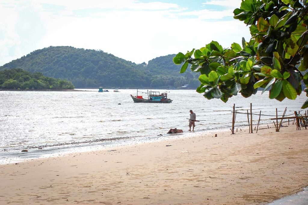 Rustig strand in Ha Tien met vissersboot op zee en groene heuvels op de achtergrond