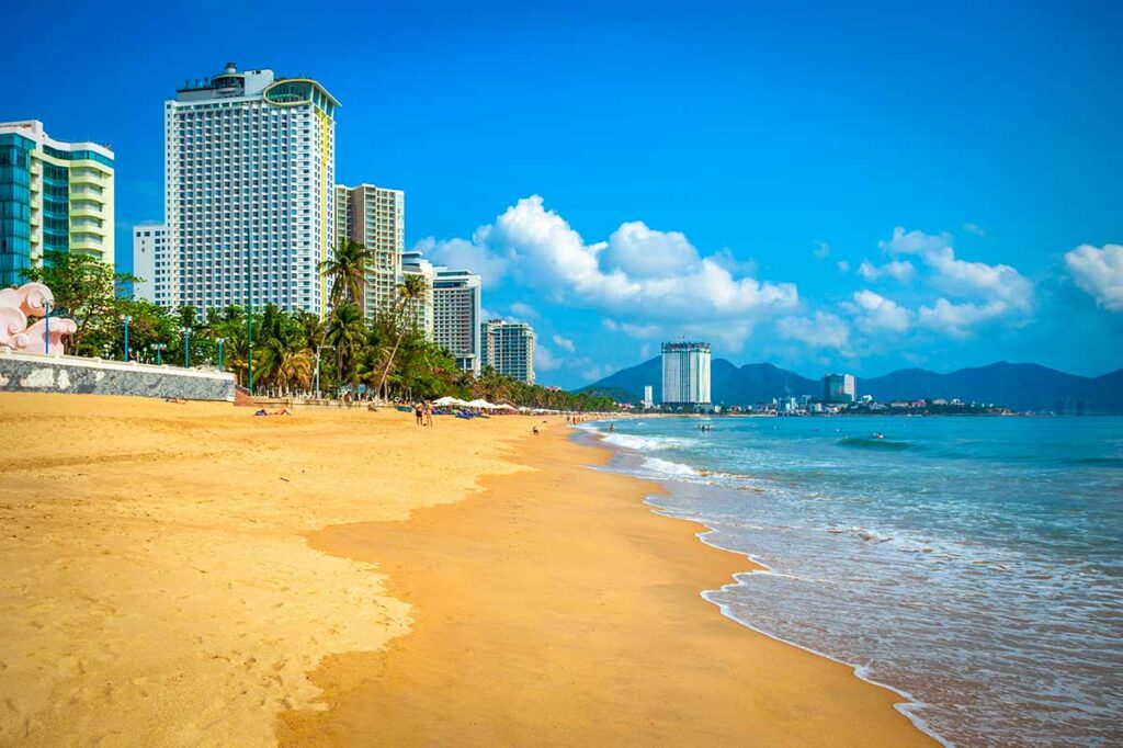 Breed zandstrand in Nha Trang met hoge hotels langs de kustlijn, rustige golven en een helderblauwe lucht op een zonnige dag