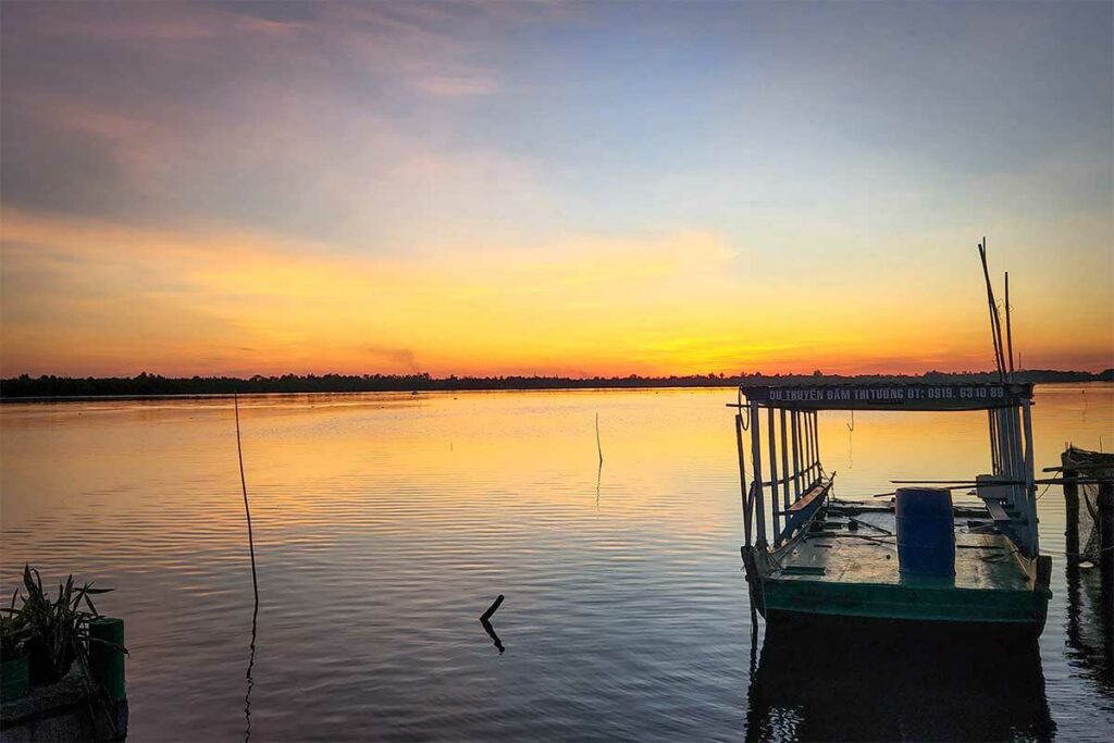 Zonsondergang boven Thi Tuong lagune in Ca Mau met vissersboot op het water