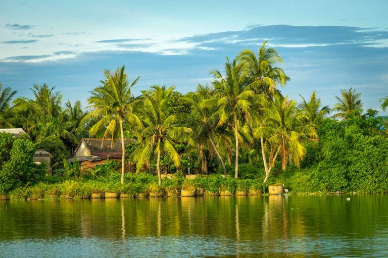 Uitzicht op de Thu Bon-rivier bij Hoi An vanaf het water, met palmbomen, traditionele huizen en groen langs de rivieroevers in centraal Vietnam