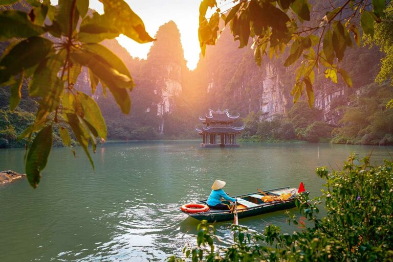 Boottocht door Trang An in Ninh Binh bij zacht ochtendlicht, met kalkstenen rotsen en tempel in het water, een klassiek beeld voor landschapsfotografie in Vietnam.