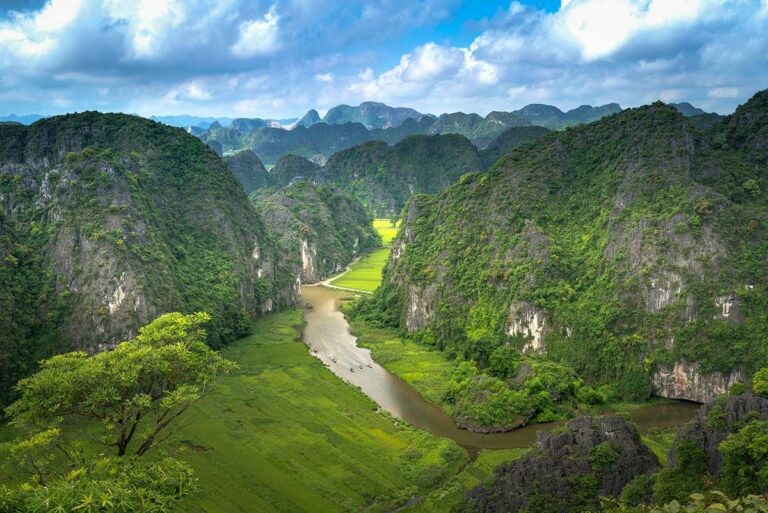 Panoramisch uitzicht vanaf Mua Cave in Ninh Binh, met kronkelende rivier, rijstvelden en steile kalksteenbergen in het Tam Coc landschap