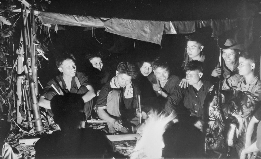 Viet Cong-soldaten zitten ’s avonds bijeen onder een eenvoudige schuilplaats in Zuid-Vietnam, ontspannen en in gesprek tijdens de Vietnamoorlog (1965).