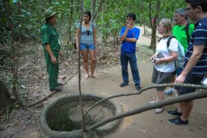 Toeristen bij een Cu Chi Tunnels ingang in de jungle bij Ho Chi Minh City terwijl een Vietnamese gids uitleg geeft over de ondergrondse tunnelopening