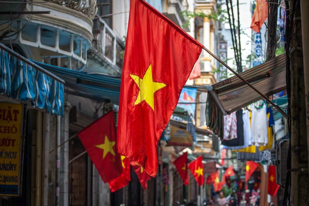 Vietnamese vlaggen hangen langs een smalle stadsstraat, bevestigd aan gevels van huizen en winkels in een woonwijk.