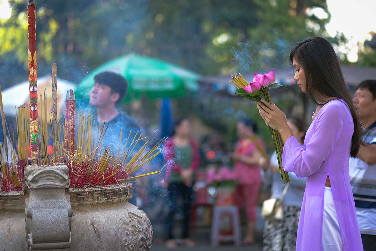 Vrouw die wierook en bloemen offert bij een tempelaltaar tijdens een religieus ritueel, typerend voor de Vietnamese volksreligie en spirituele tradities