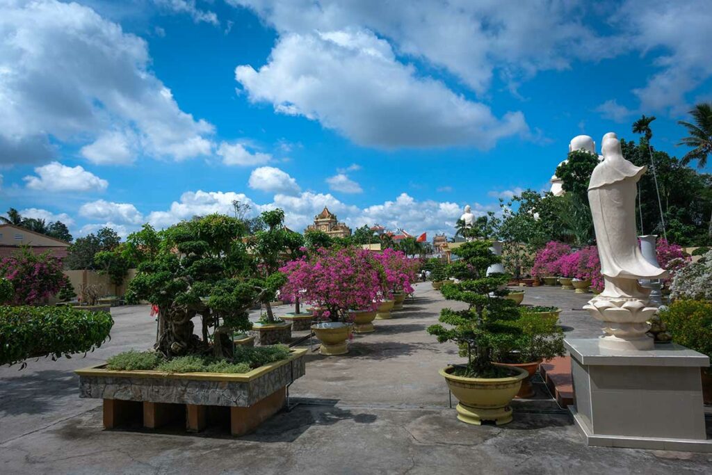 Tuin van Vinh Trang Pagoda met bonsaibomen, bloeiende struiken en wandelpaden tussen de Boeddhabeelden in My Tho
