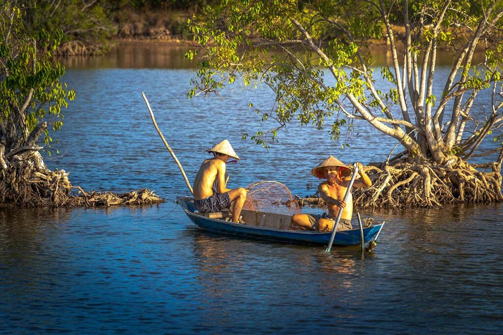 Lokale vissers in een kleine boot tussen mangrovebomen in Tra Vinh, typisch landschap van de Mekongdelta