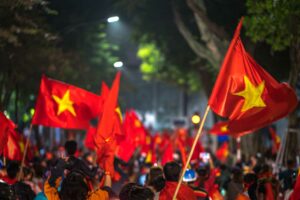 Avondviering na een voetbalwedstrijd waarbij fans de Vietnamese vlag hooghouden langs een met bomen omzoomde straat.