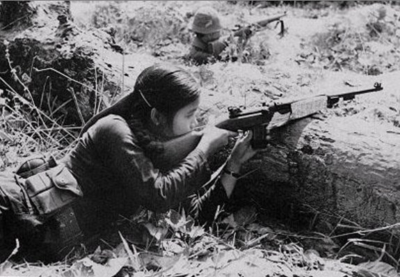 Vrouwelijke Viet Cong-guerrillastrijder ligt in dekking met een geweer, gefotografeerd tijdens de Vietnamoorlog.