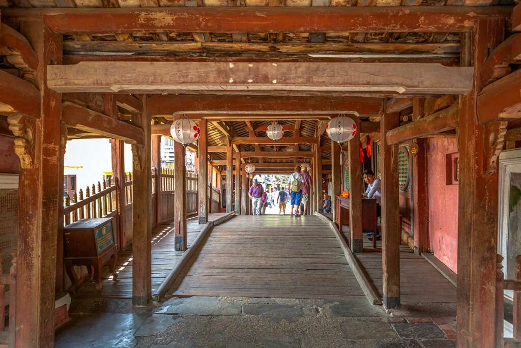 Bezoekers lopen over de houten overdekte Japanse Brug in Hoi An met lampionnen aan het plafond