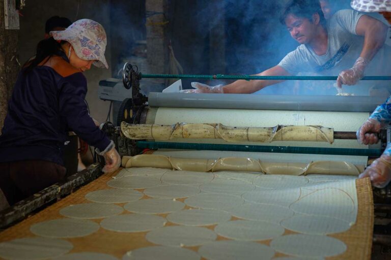 Lokale arbeiders maken traditioneel rijstpapier in een werkplaats in Ben Tre, Mekong Delta, waarbij dunne rijstvellen machinaal worden uitgerold – rijstpapier maken Mekong Delta
