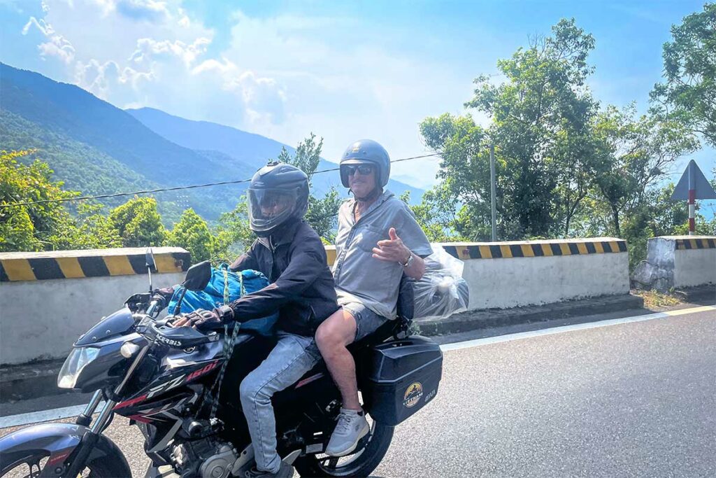 Reiziger achterop motor tijdens een Easy Rider tour op de Hai Van Pass met uitzicht op bergen en bochten in centraal Vietnam
