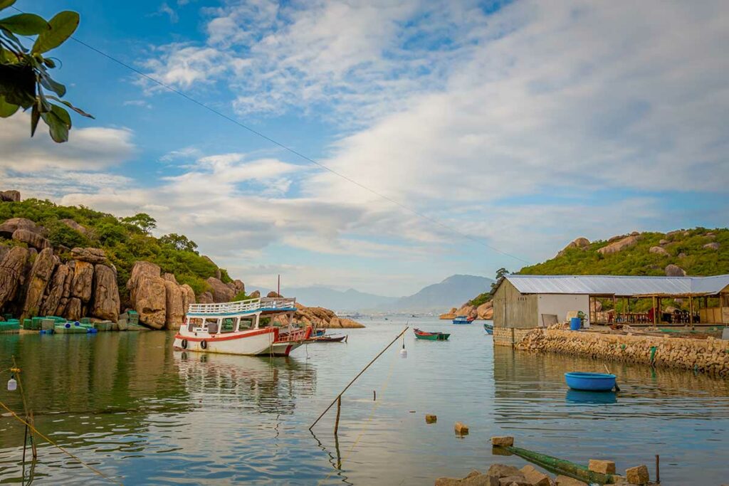 Kleine baai bij Cam Lap in Cam Ranh met vissersboten, houten huizen aan het water en omringende rotsheuvels.
