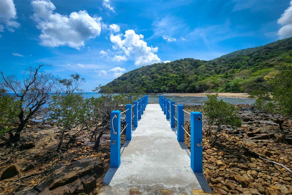 Pier bij Dat Tham Beach in Con Dao met uitzicht op ruige kustlijn, helder zeewater en beboste heuvels rondom het strand.