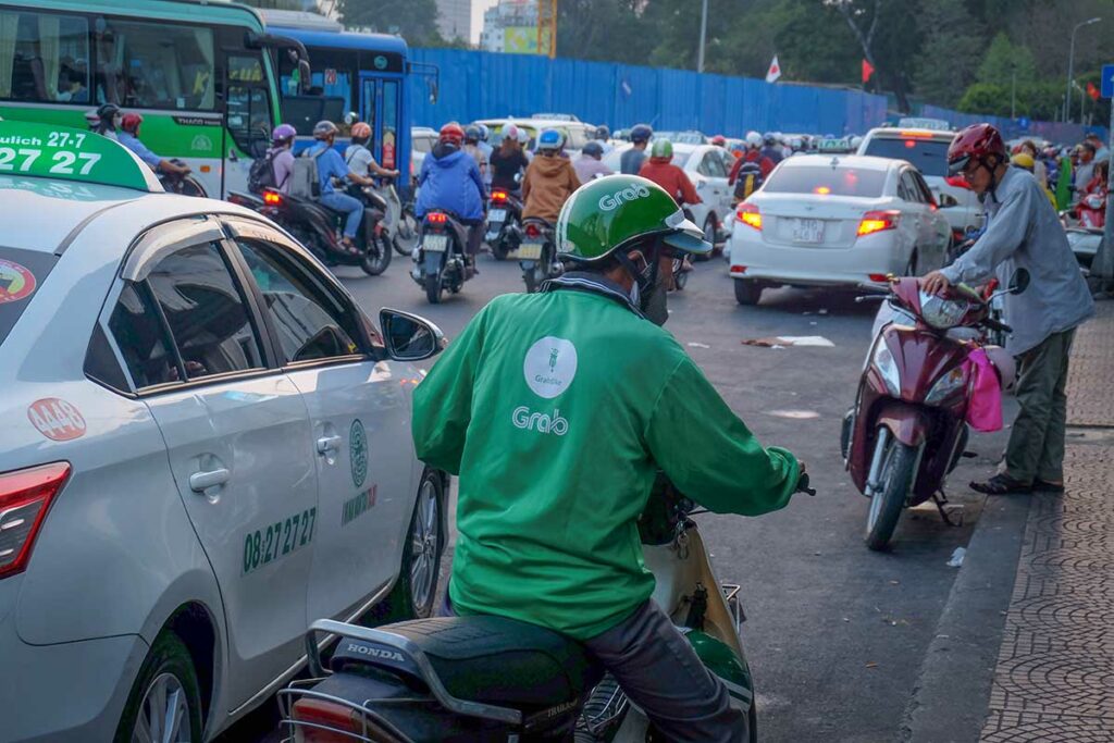 Grab motorbike taxi chauffeur in druk verkeer in Vietnam met herkenbare groene Grab jas en helm