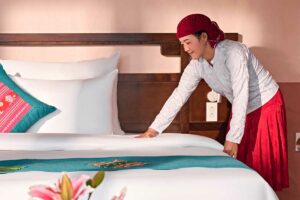 Hmong medewerker van Ha Giang Aya Lodge maakt een bed op in een kamer met traditionele details in de bergen van Ha Giang