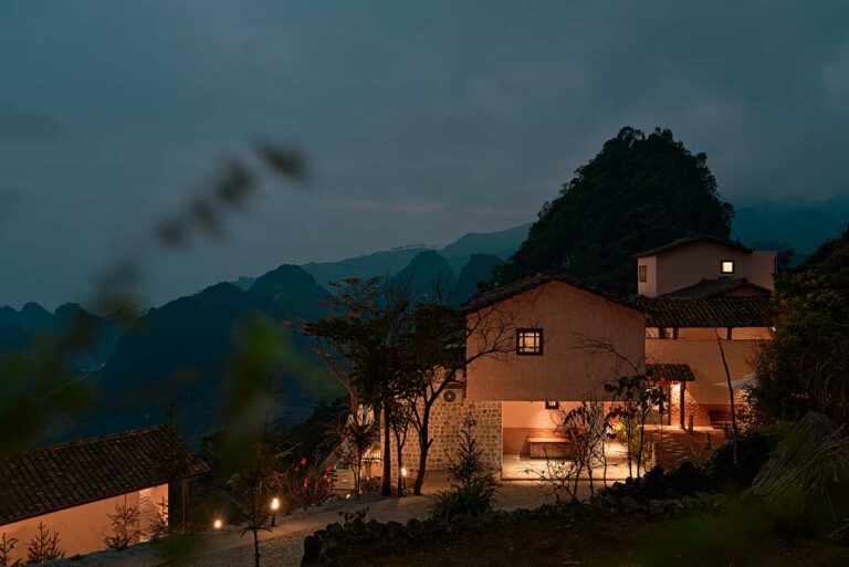 Ha Giang Aya Lodge bij avond met warme verlichting tussen de bergen van Ha Giang, uitzicht over het ruige karstlandschap van Noord-Vietnam