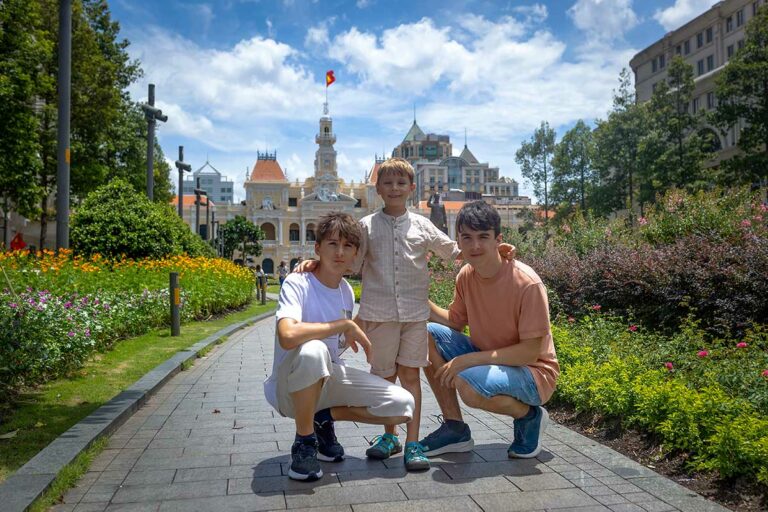 Kinderen en tieners in Ho Chi Minh City bij het stadhuis met bloemen en skyline op de achtergrond