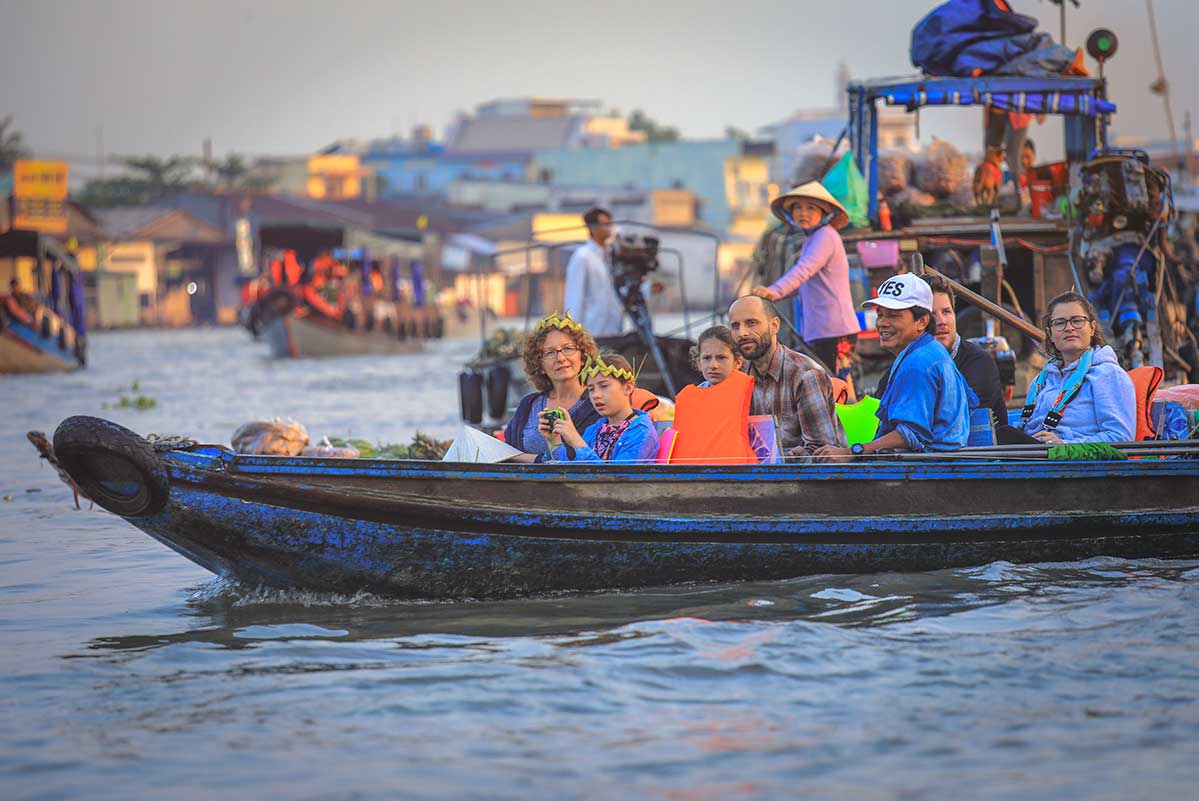 Mekong Delta met kinderen op boot bij drijvende markt met handelaren en kleurrijke boten