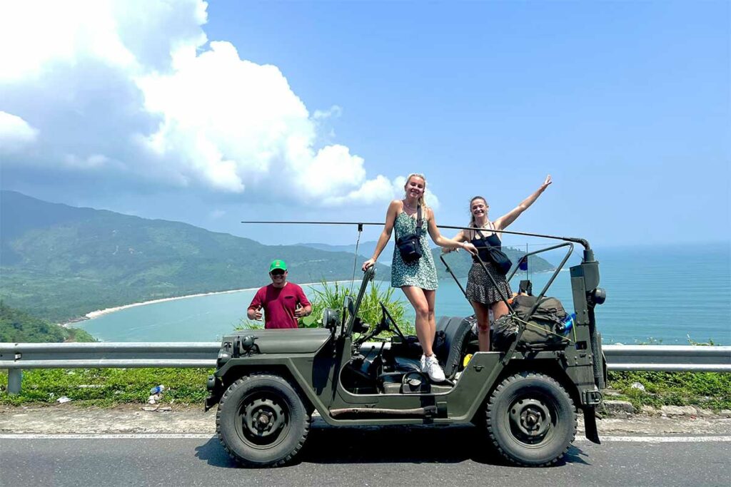 Toeristen poseren op militaire jeep tijdens Hai Van Pass tour met uitzicht op zee en bergen in Vietnam