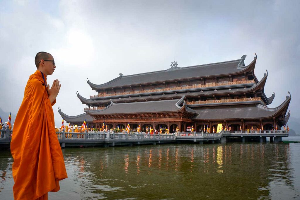 Boeddhistische monnik bij Tam Chuc Pagoda met hoofdtempel op het water en gebedsgebaar