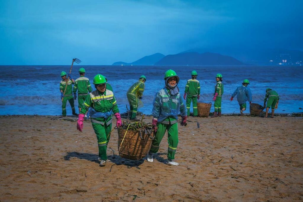 Opruimploeg ruimt afval en takken op van een strand in Vietnam na een tyfoon of zware storm