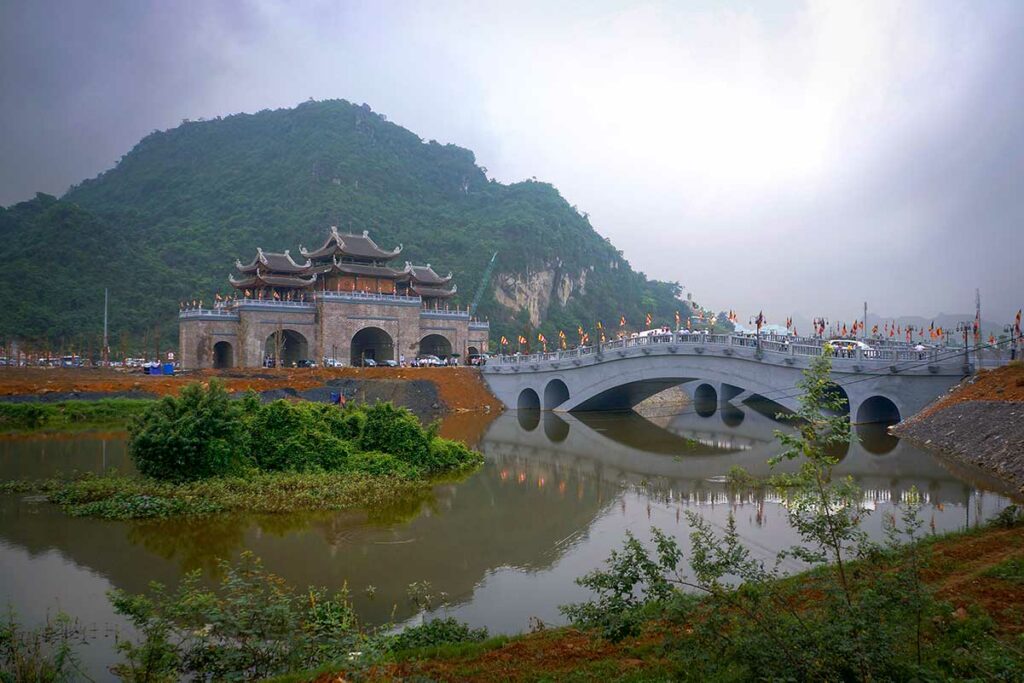 Entree van Tam Chuc Pagoda met brug, toegangspoort en parkeergebied aan het meer