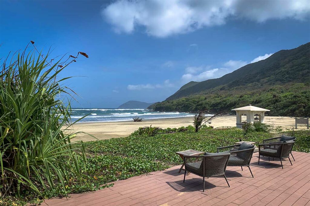 Uitzicht vanaf Poulo Condor Resort over Dong Beach in Con Dao met ligstoelen, groen begroeide kust en een breed zandstrand langs de bergen.