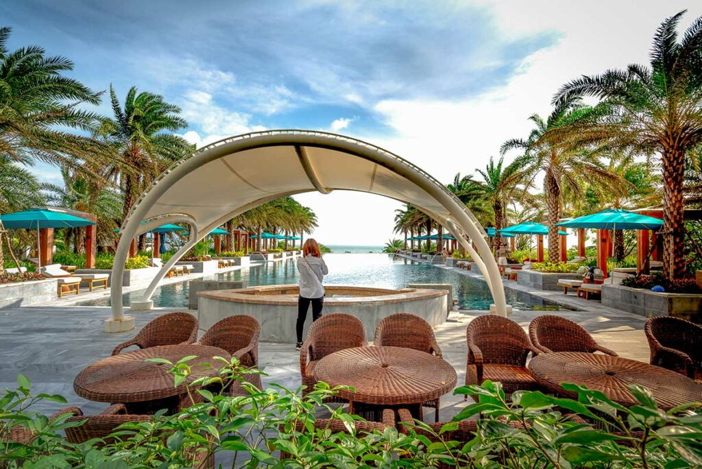 Zwembad van Radisson Blu Resort Cam Ranh met ligbedden, palmbomen en uitzicht richting het strand.