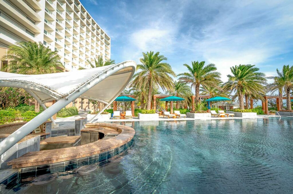 Luxe zwembad bij Radisson Blu Resort Cam Ranh met zonneterrassen, palmbomen en hotelgebouw op de achtergrond.