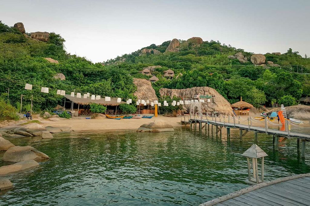 Kleinschalig resort aan het strand op het Cam Lap-schiereiland in Cam Ranh, met houten pier en rustige baai omringd door groene heuvels.