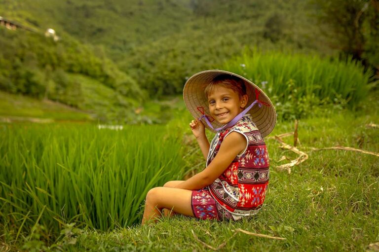 Kind in traditionele kleding met Vietnamese hoed tussen groene rijstvelden in Sapa