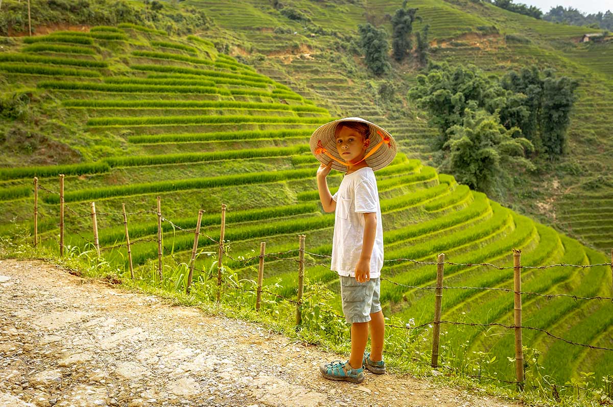 Kind met Vietnamese hoed tijdens trekking langs terrasvormige rijstvelden in Sapa