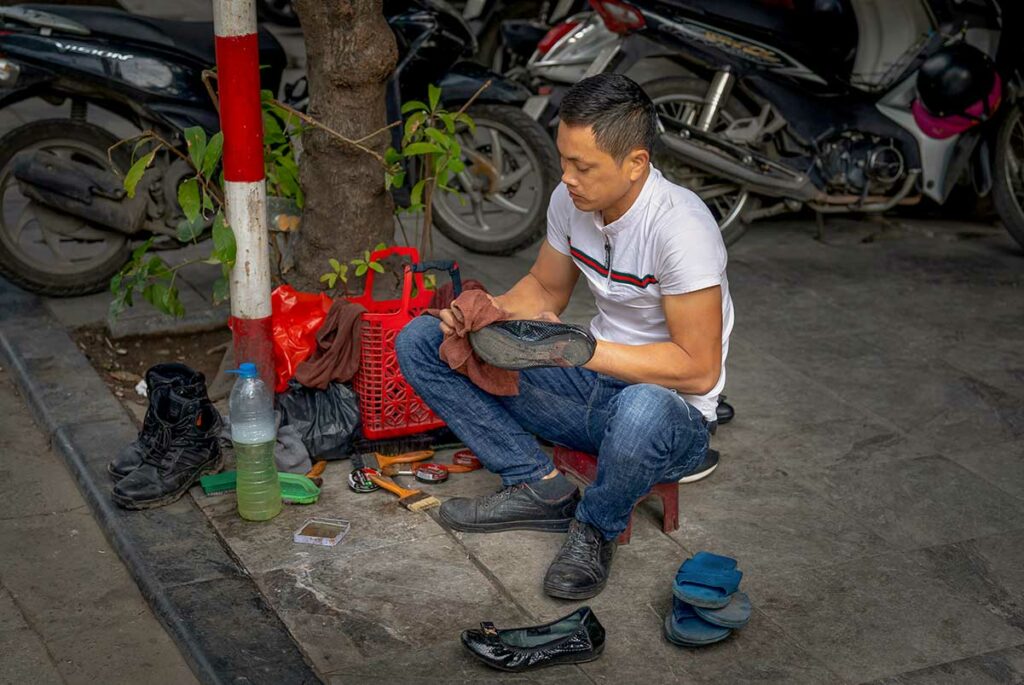 schoenenpoetser op straat in Hanoi die schoenen schoonmaakt voor voorbijgangers