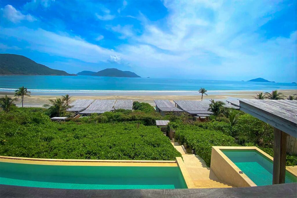 Luxe uitzicht vanaf Six Senses Con Dao over Dat Doc Beach met privévilla’s, infinity pool en een lang zandstrand aan een rustige baai.