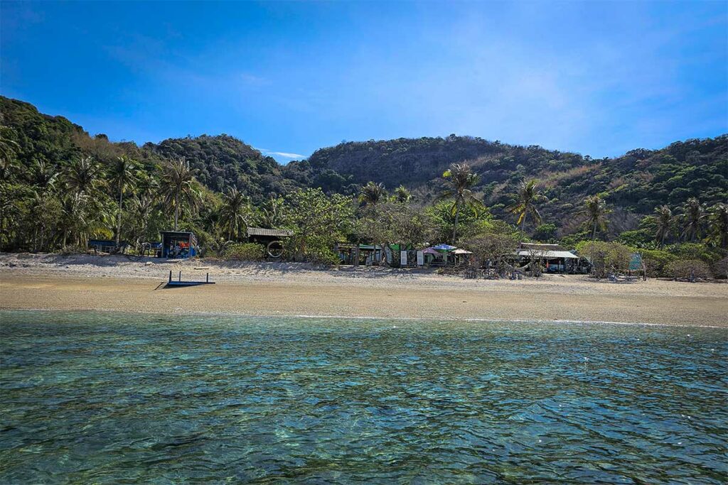 Rustig strand op Hon Cau Island in Con Dao met helder water, zandstrand en eenvoudige strandhutten aan de rand van de jungle.