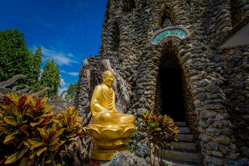 Boeddhabeeld bij Tu Van Pagoda in Cam Ranh met ingang van de schelpenpagode op de achtergrond.