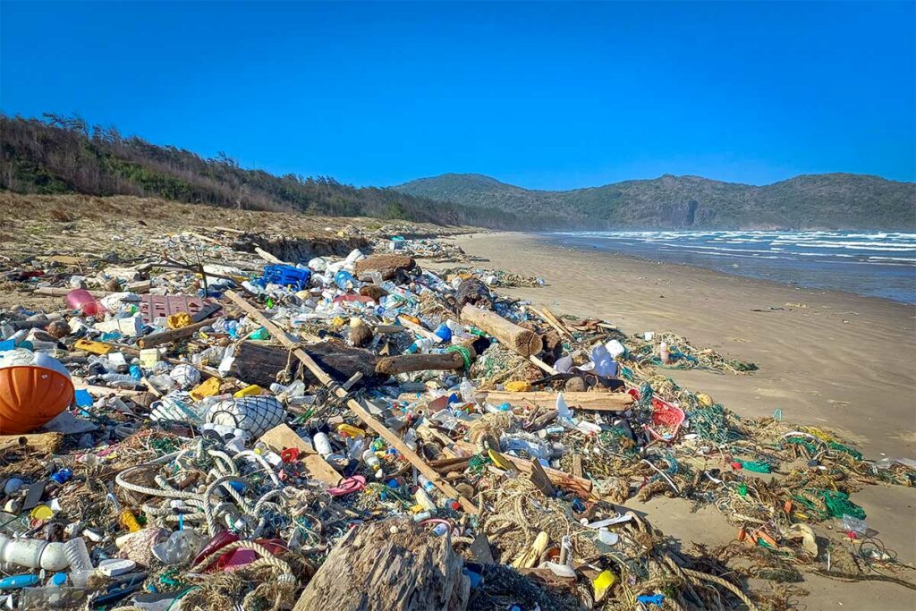 Vervuild deel van Dong Beach in Con Dao met aangespoeld plastic en afval langs het strand, met bergen en zee op de achtergrond.