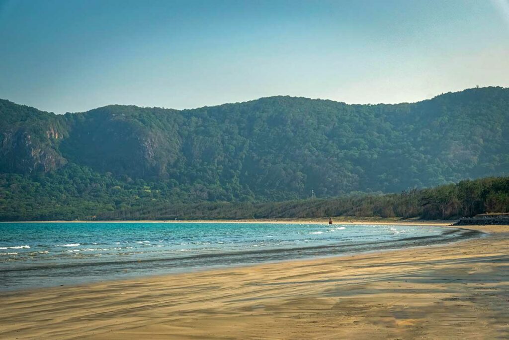 Langgerekt strand van Bien Dong Beach in Con Dao met rustige zee, brede zandvlakte en groene bergen op de achtergrond.