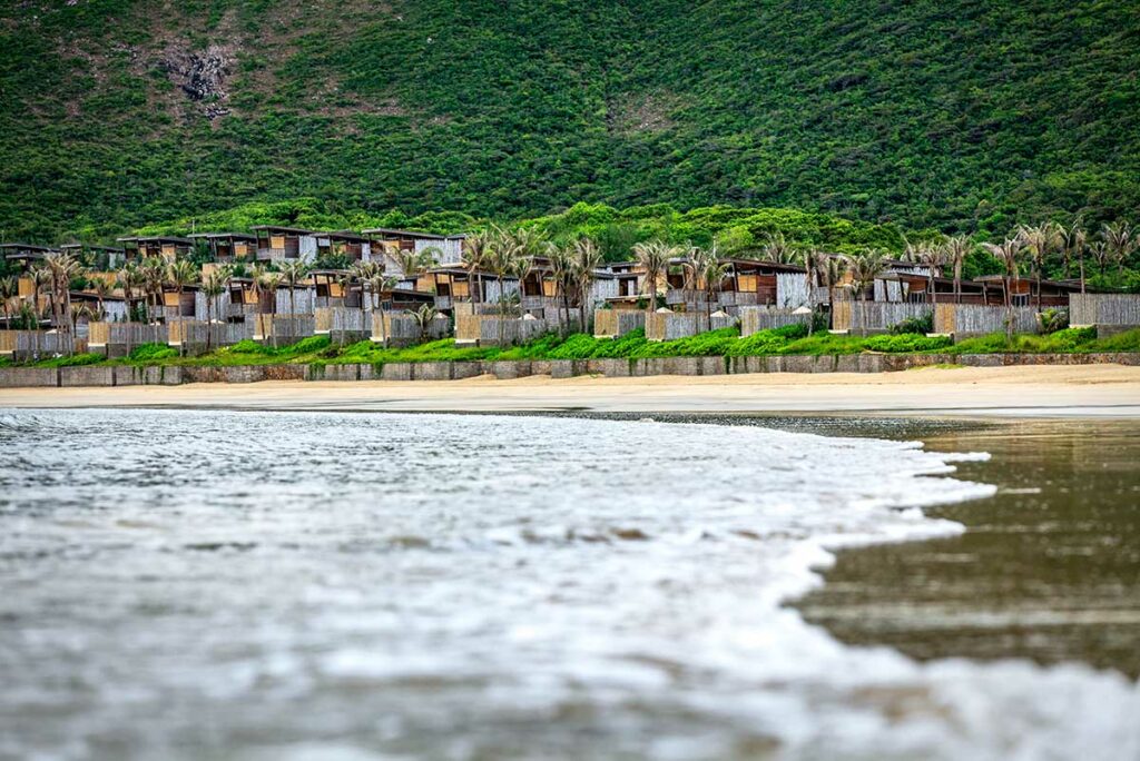 Strand bij Six Senses Con Dao met luxe villa’s aan Dat Doc Beach, rustig water en groene bergen op de achtergrond.
