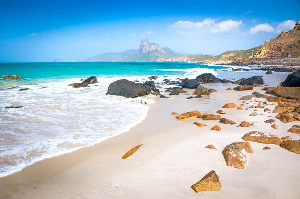 Rotsachtig strand van Nhat Beach in Con Dao met helder turquoise water, grote stenen en uitzicht op de bergen langs de kust.