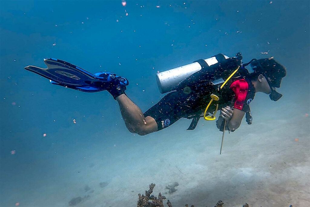 Scuba duiker met volledige uitrusting zwemt boven de zandbodem tijdens een duik in Con Dao, met rustig water en goed zicht.