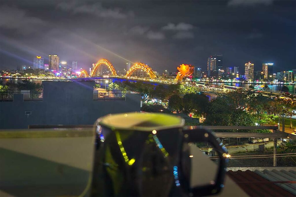 Uitzicht vanaf een rooftopbar in Da Nang op de verlichte Dragon Bridge in de avond, met de brug en skyline langs de Han River op de achtergrond.
