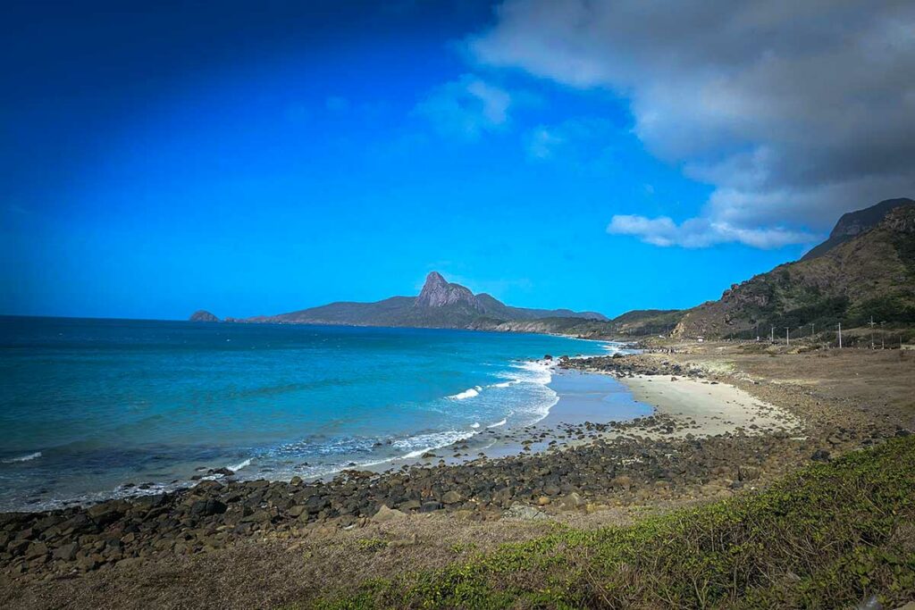 Uitzicht vanaf Nhat Beach in Con Dao met ruige kustlijn, helder water en bergen op de achtergrond.
