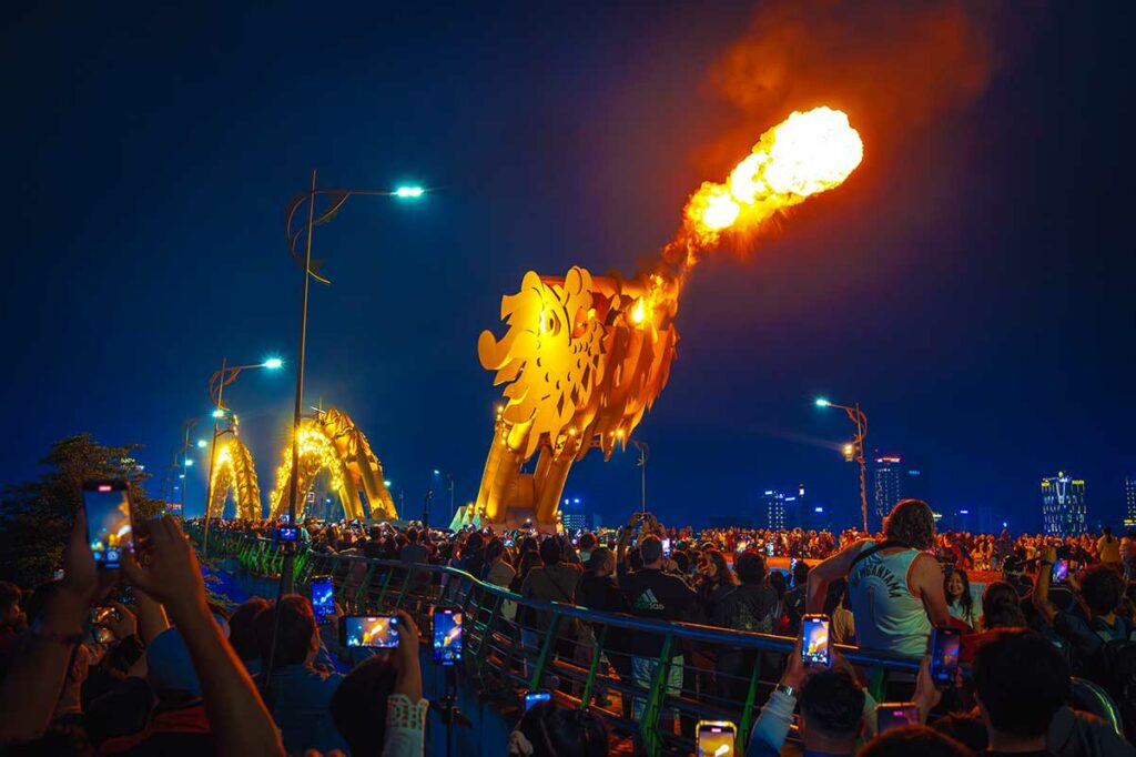 Dragon Bridge in Da Nang tijdens de vuurshow, waarbij de drakenkop vuur spuwt boven een grote menigte toeschouwers op de brug.