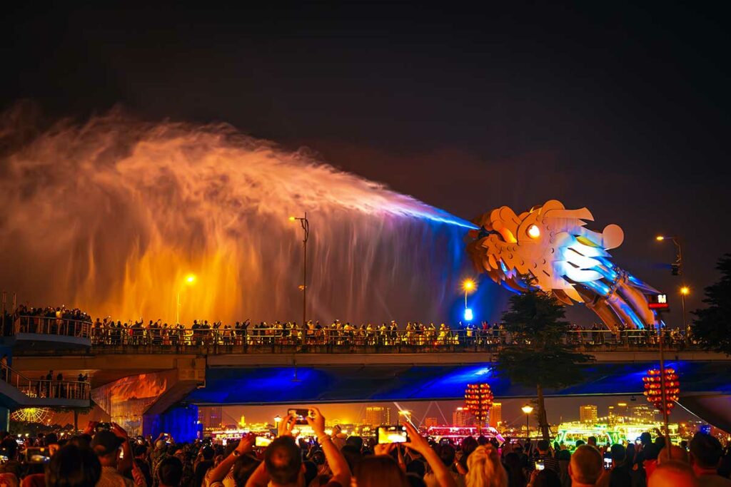 Dragon Bridge in Da Nang tijdens de watershow, waarbij de drakenkop een krachtige waterstraal over de brug en het publiek sproeit.